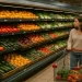A woman shopping in a grocery store produce aisle, showing the abundance that hides the impact of chemical farming on soil health.