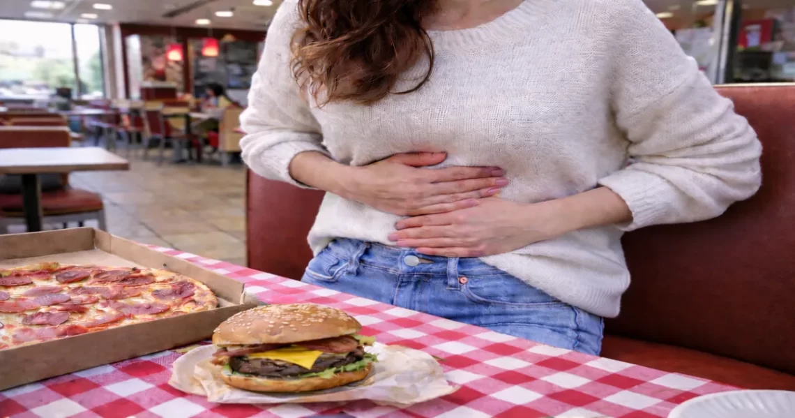 Woman holding her stomach after eating fast food, showing how stress and unhealthy food choices can trigger gut discomfort