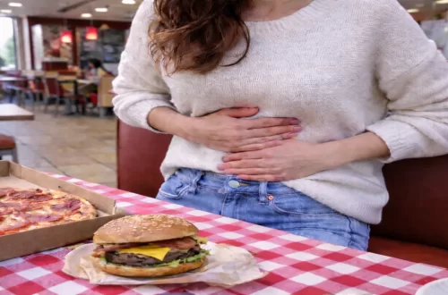 Woman holding her stomach after eating fast food, showing how stress and unhealthy food choices can trigger gut discomfort