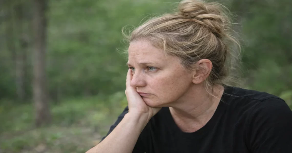 Woman sitting outdoors in natural light looking thoughtful and grounded, representing nervous system regulation and emotional safety