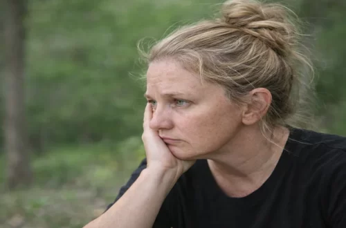 Woman sitting outdoors in natural light looking thoughtful and grounded, representing nervous system regulation and emotional safety
