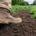 Farmer’s boot stepping into rich living soil between rows of green crops, showing the connection between farmland health and the human microbiome