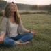 Woman sitting cross-legged in grass at sunrise with eyes closed, reflecting body awareness and health intuition