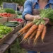 Person holding freshly harvested carrots at a local farmers market with vegetables displayed in the background