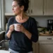 woman standing in kitchen looking out window holding coffee thinking about health changes
