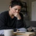 Woman sitting on a couch looking stressed while thinking with a notebook and laptop nearby, representing difficulty with change and decision-making