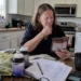 A woman sits at a kitchen table looking confused while comparing food labels, supplement bottles, notes, and health information, showing how conflicting health advice can feel overwhelming.
