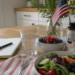 Lightly patriotic kitchen table scene with healthy food, water, supplements, a notebook, and a small American flag representing health independence at home.