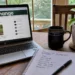 Laptop showing the A Voice For Change website beside a notebook, coffee mug, and houseplant in a natural home workspace