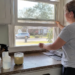 Woman opening her kitchen window near common household products that can contribute to everyday toxin exposure.