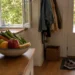 An open kitchen window, bowl of fresh produce, glass of water, and walking shoes by the door show how daily surroundings can support health.