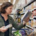 Woman comparing packaged food labels in a grocery aisle before deciding what to buy
