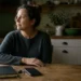 Middle-aged woman pausing at her kitchen table with her phone facedown, representing nervous system regulation and recovery from stress.