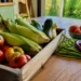 Fresh seasonal tomatoes, sweet corn, zucchini, peppers, peaches, and green beans arranged on a wooden kitchen table.
